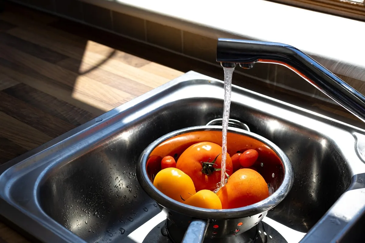 Légumes frais rincés sous l'eau courante dans un évier de cuisine