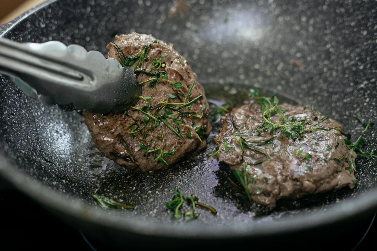 Viande congelée cuisant dans une poêle chaude avec de la vapeur et une croûte dorée
