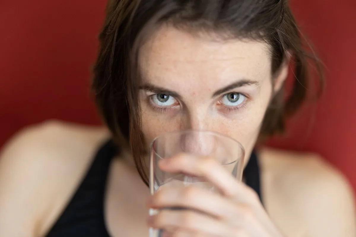 Femme buvant de l'eau régulièrement, illustration de l'hydratation quotidienne pour prévenir les récidives