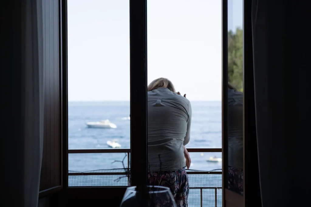 Personne assise près d'une fenêtre ensoleillée, l'air préoccupé, illustrant la dépression estivale.