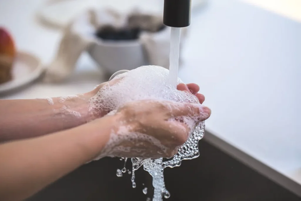 Mains savonnées sous l'eau chaude dans une douche lumineuse et tropicale