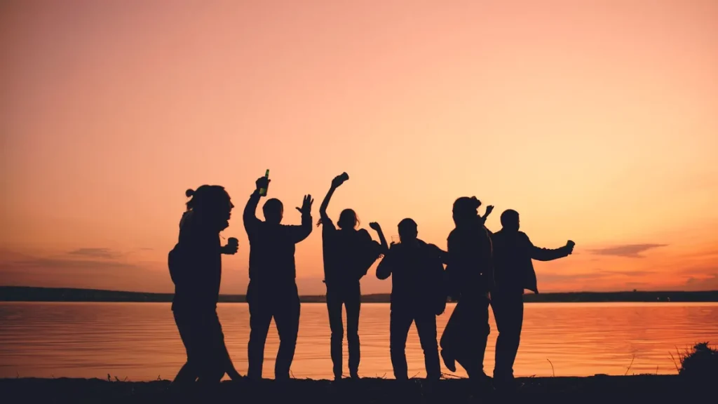 Groupe de jeunes silhouettes dansant lors d'une fête estivale en bord de mer au coucher du soleil.