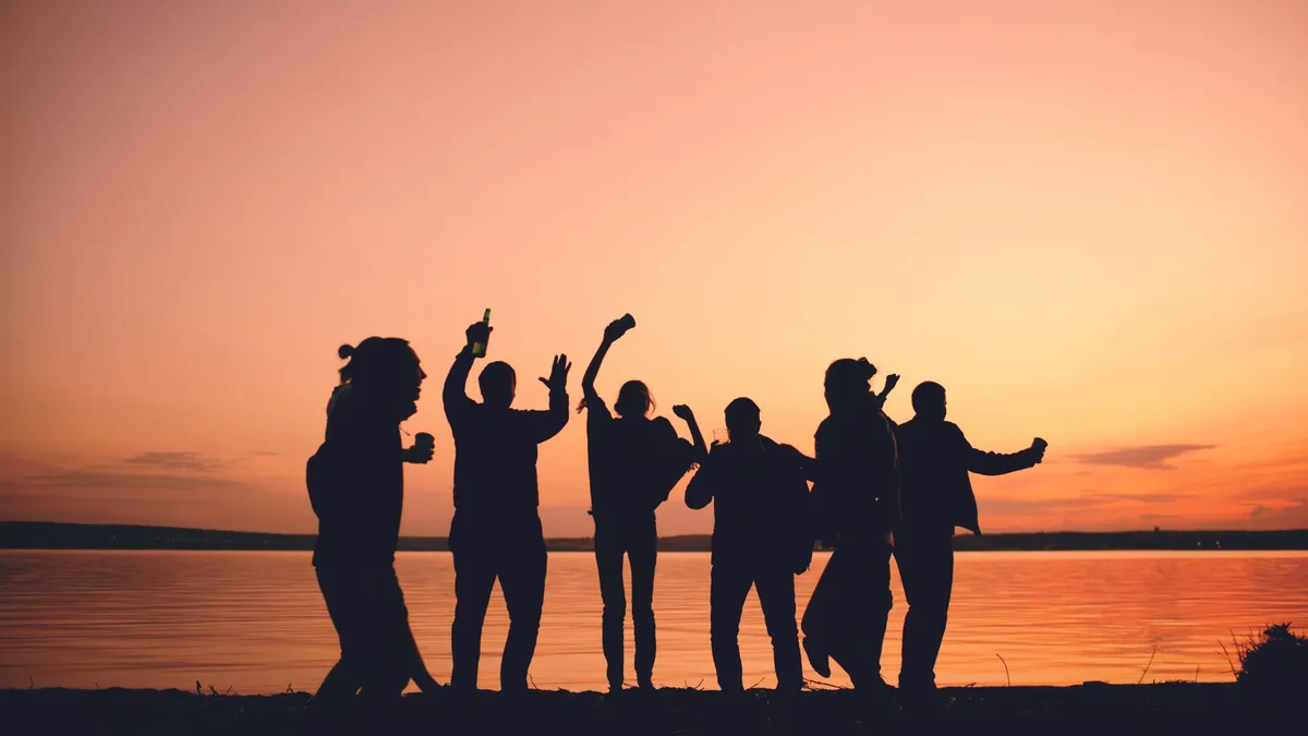 Groupe de jeunes silhouettes dansant lors d'une fête estivale en bord de mer au coucher du soleil.