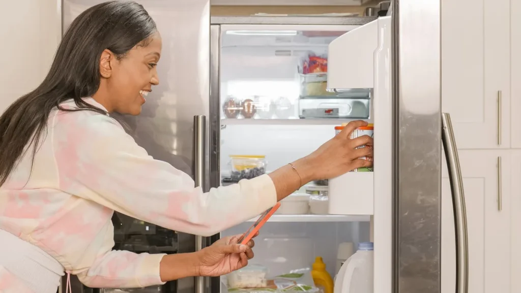 Mains tenant un emballage alimentaire au-dessus d'un réfrigérateur avec avis de rappel en arrière-plan