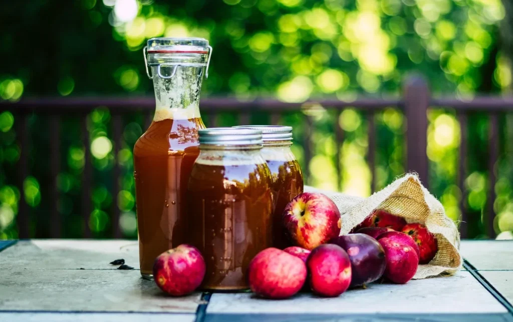 Verre de vinaigre de cidre dilué près de pommes fraîches sur un plan de travail de cuisine