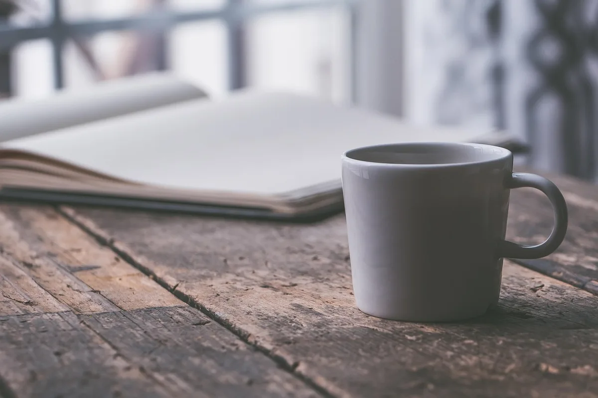 Tasse et carnet sur un rebord de fenêtre ensoleillé avec un diffuseur et des bouchons d'oreille flous en arrière-plan