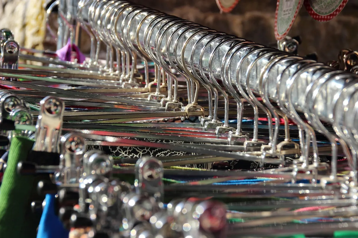Mains fouillant un portant de vêtements en boutique de friperie